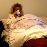 a woman sick in bed sipping a cup of herbal tea